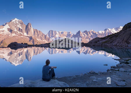 Female traveler looking the Alps mountain range at sunset with beautiful reflection in a lake, near Chamonix and the White Mount Stock Photo
