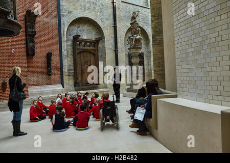 London, Group of pupils sitting on the floor listen the guide in Victoria and Albert Museum is the world’s largest museum of decorative arts. Stock Photo