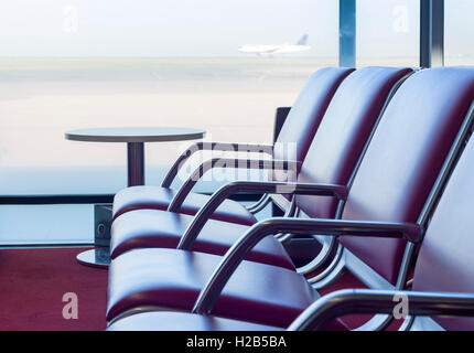 Bench in departure flights waiting hall at the airport with airplane in the background Stock Photo