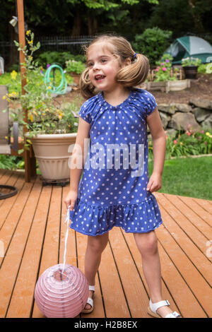 Three year old girl playing with a paper lantern on a cedar wood deck in Issaquah, Washington, USA Stock Photo