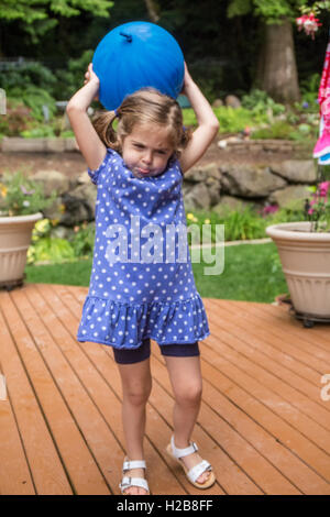 Three year old girl playing with a balloon, looking like she is struggling, in Issaquah, Washington, USA Stock Photo