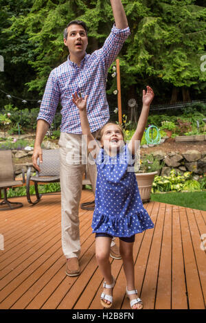 Three year old girl trying to catch a balloon, with her father behind her, in Issaquah, Washington, USA Stock Photo