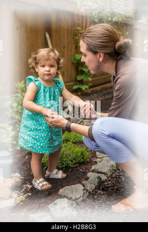 Thirty-four year old mother holding eighteen month old daughter's hands as she stands in a backyard garden Stock Photo