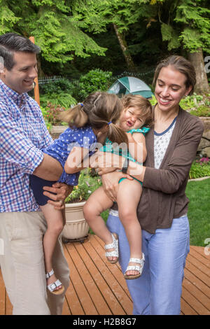 Thirty-four year old parents holding their three and one year old daughters as one tries to kiss the other Stock Photo