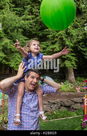 Thirty-four year old father holding his three year old daughter as she catches a balloon tossed to her Stock Photo