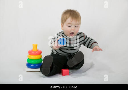 10.5 month old toddler boy playing with plastic toys, being very wobbly as he reaches for another toy Stock Photo