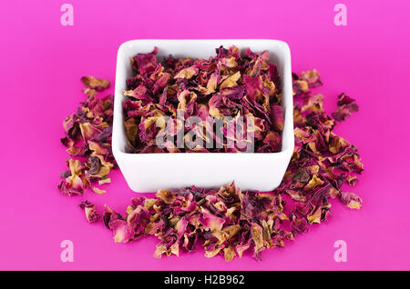Rose petals in a white bowl on pink background. Dried blossoms, used for perfumes, cosmetics, teas and baths. Stock Photo