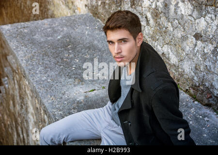 Portrait of good-looking man sitting on stone edge Stock Photo