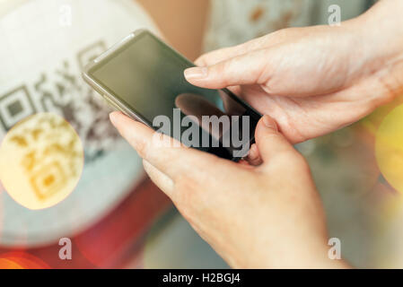 Woman scanning QR code on outdoor advertising billboard with smartphone Stock Photo