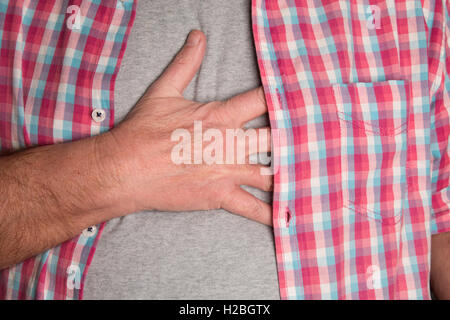 A man presses his hand against his chest whilst he is suffering from pain. Stock Photo