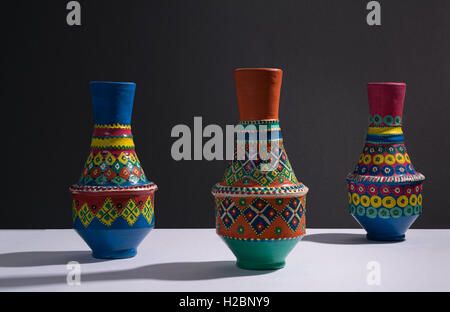 Still life of three artistic painted colorful handcrafted pottery vases with harsh shadow on white table and black wall Stock Photo