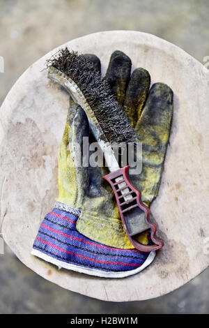 Dirty worker's glove holding a wire brush on a wooden plank in a workshop Stock Photo