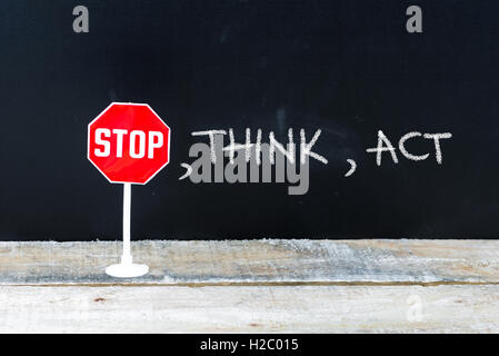 Mini STOP sign over chalkboard background and table, STOP, THINK, ACT concept Stock Photo