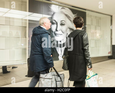 People walking past H&M store with image of mature woman in store window in Trinity Leeds shopping centre. Leeds, England. UK Stock Photo