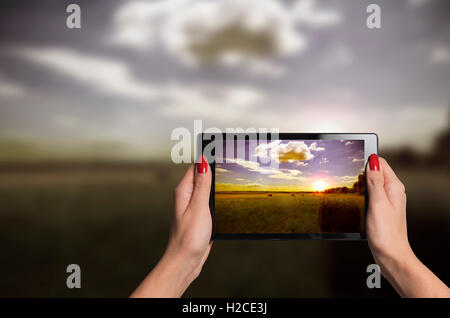 hands holding a tablet taking beautiful photographs of nature in sunset improving vision Stock Photo
