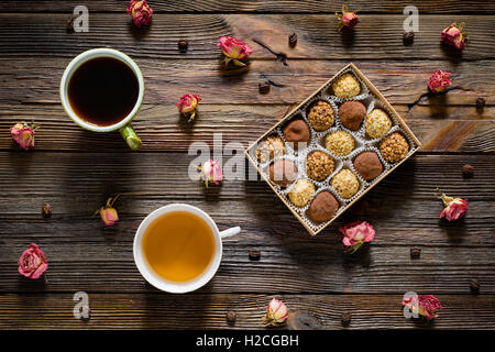Sweet food pattern. Box of chocolate truffles, coffee beans, dry rose flowers, cup of black coffee and green tea on wooden table Stock Photo