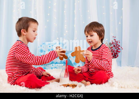 Two happy children eating cookies at christmas and drinking milk, laughing and talking, having fun Stock Photo