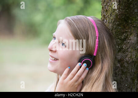 Girl Sitting Against Tree In Garden Listening To Music On Headphones Stock Photo