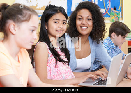 Teacher Helping Group Of Elementary School Children In Computer Class Stock Photo