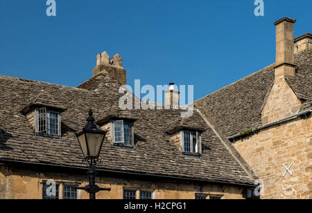 Old Cotswold stone tiled roof with dormer windows, chimneys and old fashioned street lamp Stock Photo