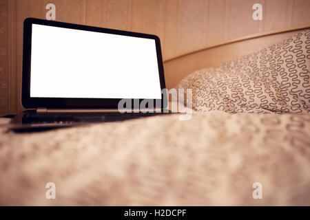 Open laptop PC on the warm toned defocused laid bed. Blank copy space on the screen, clipping path included. Stock Photo