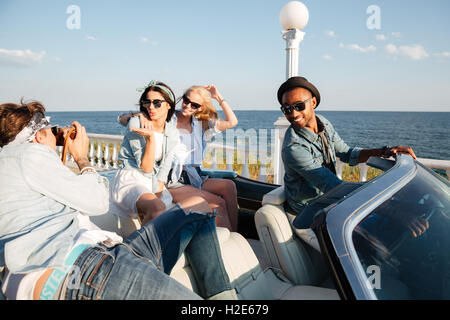 Multiethnic group of happy young people taking photos in cabriolet in summer Stock Photo