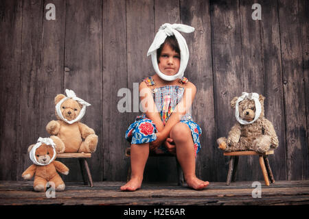 Four-year girl and teddy bears with toothache, sitting in front of wooden hut