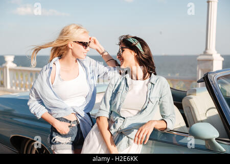 Two happy pretty young women standing and talking near cabriolet Stock Photo