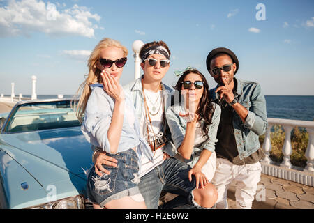 Multiethnic group of happy young people standing and sendng kisses near vintage cabriolet in summer Stock Photo