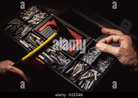 Old suitcase for nails, anchors and screws and one hand holding a hammer while the other hand choosing a right nail. Stock Photo