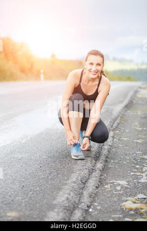 Young fitness woman tying her shoes before jogging on road Stock Photo