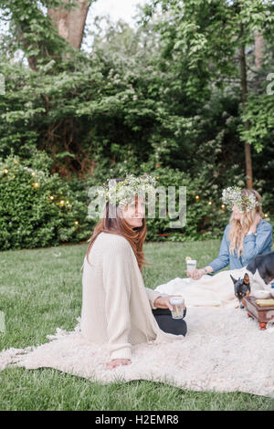 Two smiling women with a flower wreaths in their hair sitting in a garden. Stock Photo