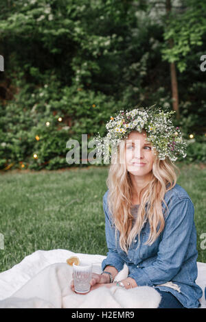 Smiling woman with a flower wreath in her hair sitting in a garden. Stock Photo