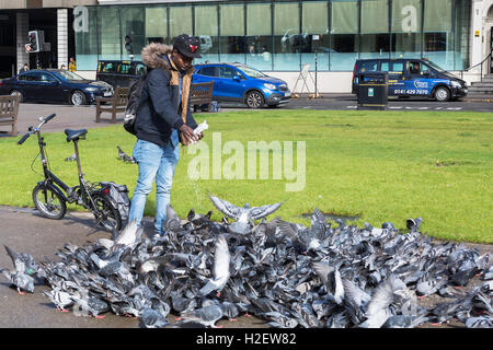 Glasgow, Scotland, UK. 27th September, 2016. YAGOUB ABDULLAH, age 25, student and (legal) refugee from Sudan, most lunch times, can be seen in George Square, Glasgow, feeding the city's pigeons with rice grains he buys from his local store. He claims that the pigeons now recognize him when he cycles into the Square, flock around him and have become so tame that they perch on him while feeding. Credit:  Findlay/Alamy Live News