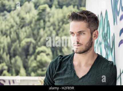 Attractive young man leaning against colorful graffiti wall, looking at camera Stock Photo
