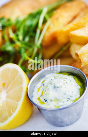 Freshly cooked chips on  a plate with garnish and tartare sauce and a cut lemon . Stock Photo
