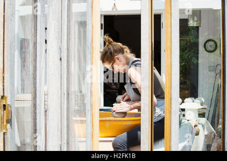 A woman potter working clay on  a potter's wheel in her workshop. Stock Photo