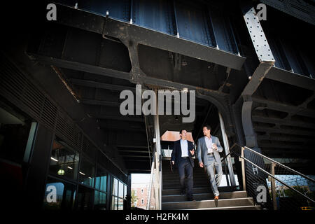 Two businessmen wearing grey suits walking down a staircase at the entrance of a building. Stock Photo