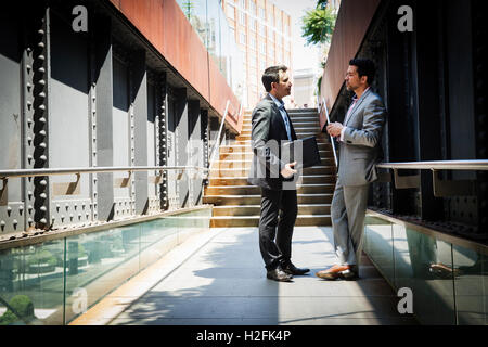 Two businessmen wearing grey suits walking down a staircase at the ...