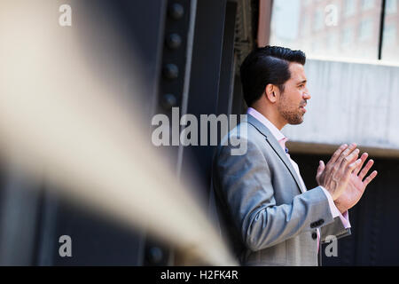 Businessman wearing a grey suit standing outdoors, talking and gesturing with his hands raised. Stock Photo