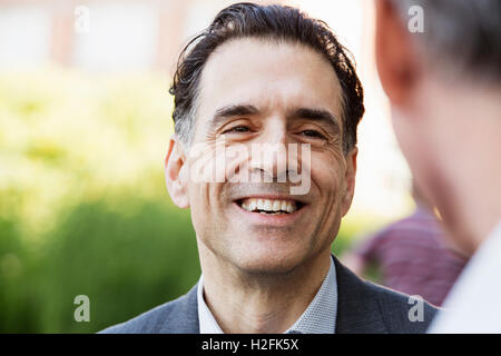 Two men talking to each other, one smiling, one unrecognizable person , Stock Photo