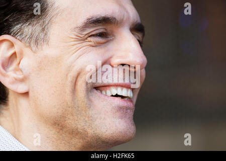 A man with greying hair in a shirt, looking sideways, smiling. Stock Photo