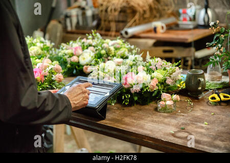 A woman in a florist's workshop using a digital tablet, at a workbench with flower arrangements. Stock Photo
