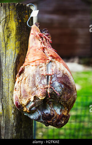 Close up of a cured ham hanging on  a wooden fence. Stock Photo