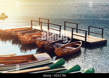 Small wooden boats and canoes docked and tied to empty pier on the lake Stock Photo