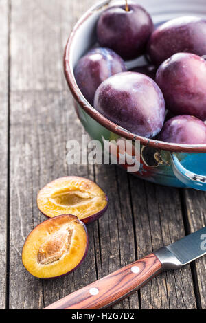 Halved ripe plums and knife on old wooden table. Stock Photo