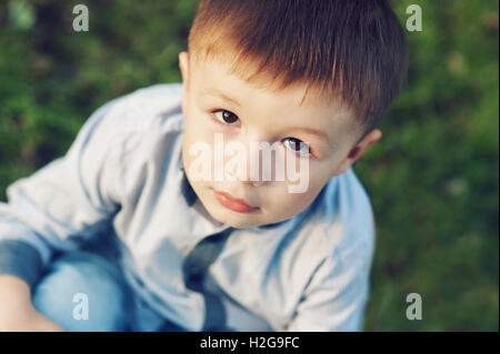 little boy sitting on the grass in park outdoors Stock Photo