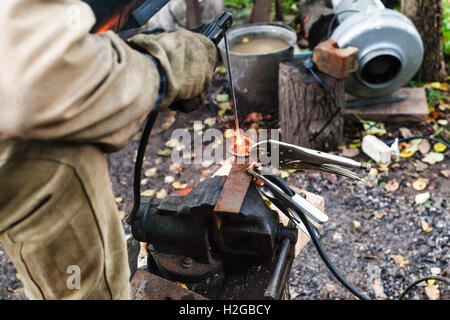 Welder welds iron ring by spot electric welding in outdoor rural workshop Stock Photo