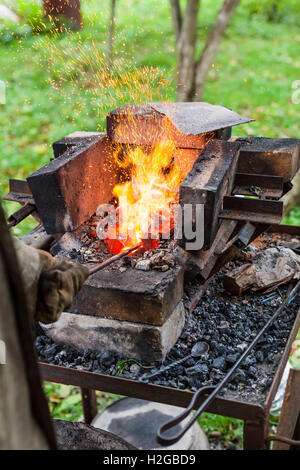 Blacksmith heats iron rod in rural forging furnace with burning coals Stock Photo