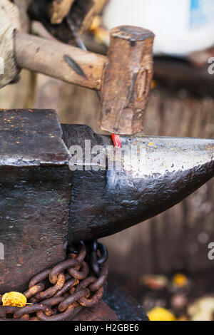 Blacksmith forges sizzling hot metal rod with sledgehammer on anvil in outdoor rural smithy Stock Photo